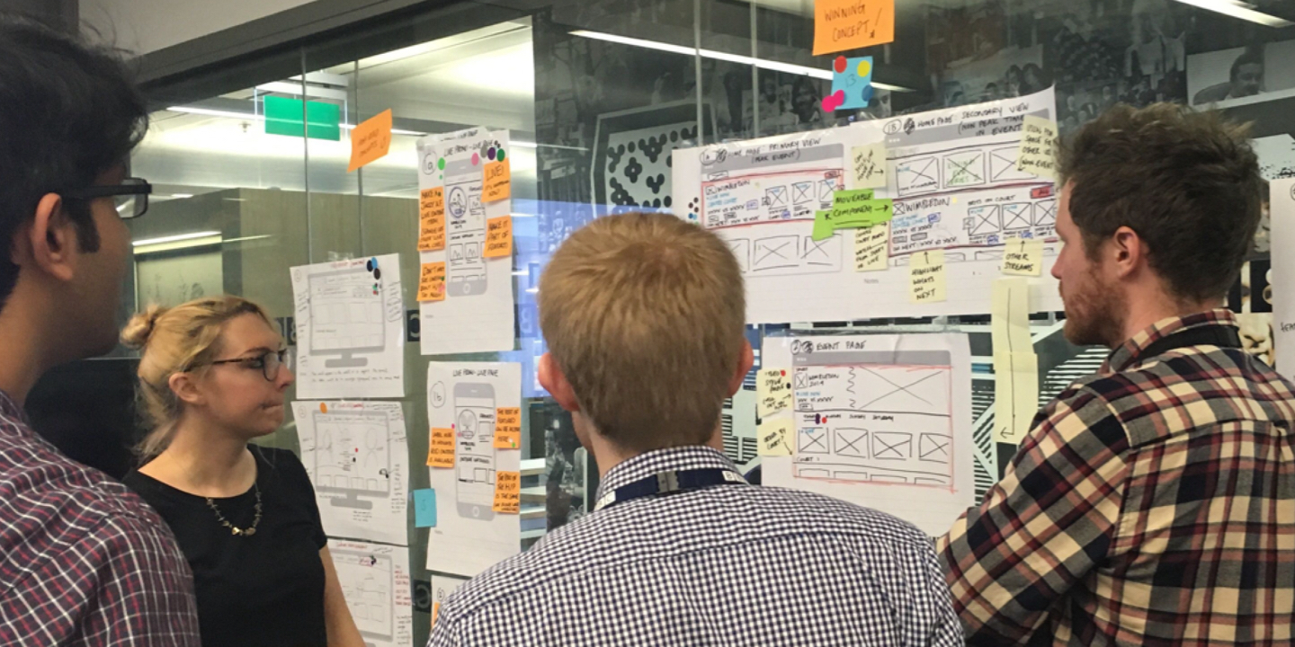 A group of people evaluating ideas pinned to a wall - everyone appears to be in deep thought